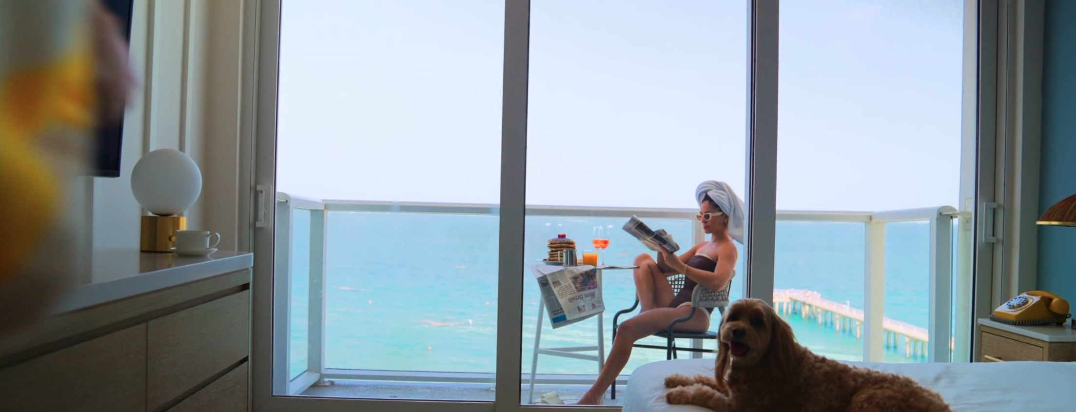1. A woman sits on a deck reading a book, while a dog relaxes on the bed.